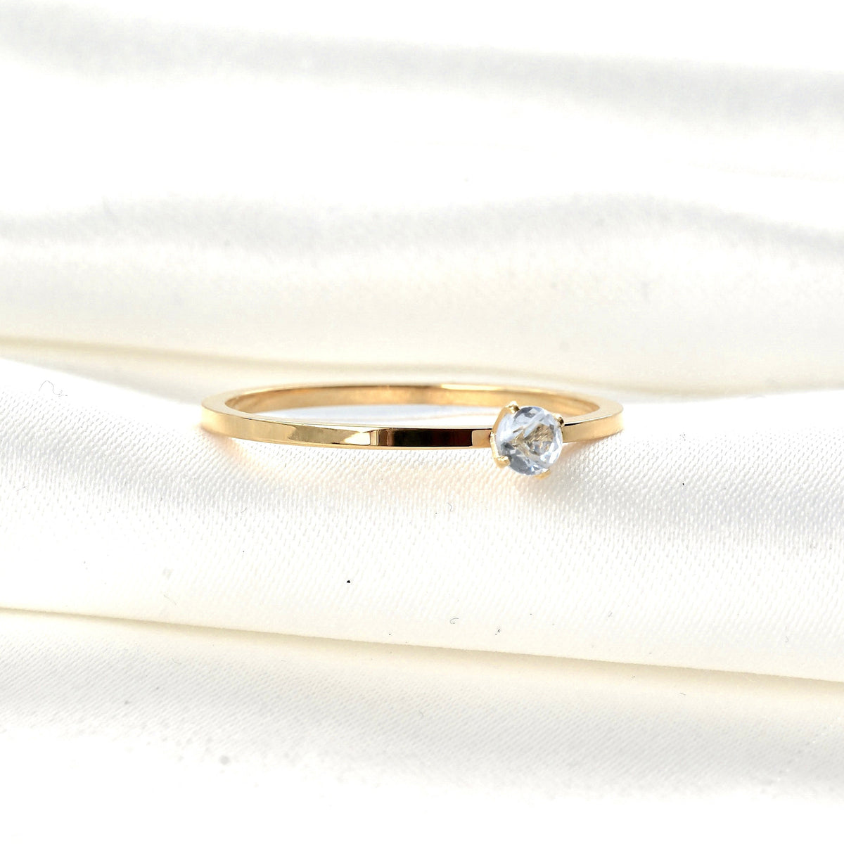 Gold solitaire ring with a clear CZ in a four prong setting on a white fabric background