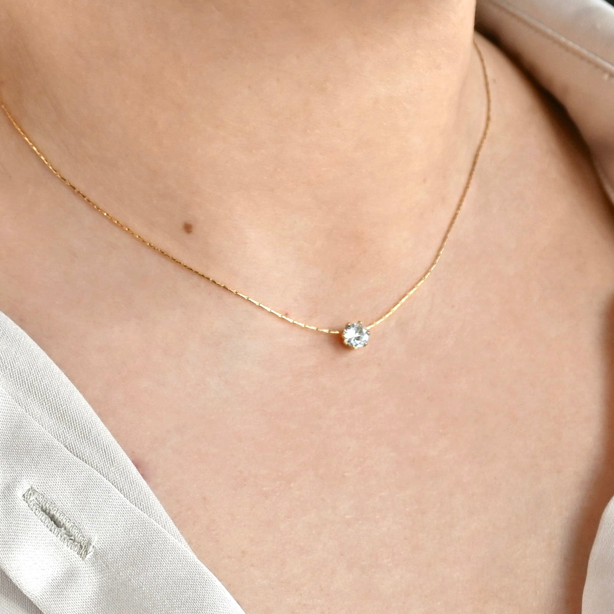 Gold necklace with a small CZ stone on a person wearing a white top.