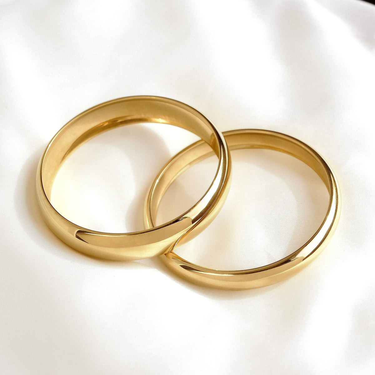Two polished gold bangle bracelets resting on a soft white fabric background.
