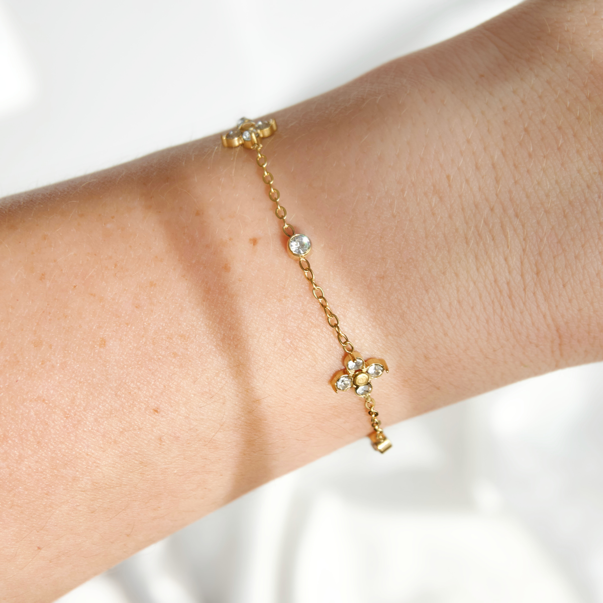 A delicate gold chain bracelet with small clear crystal accents, shown worn on a person's wrist against a soft white background.