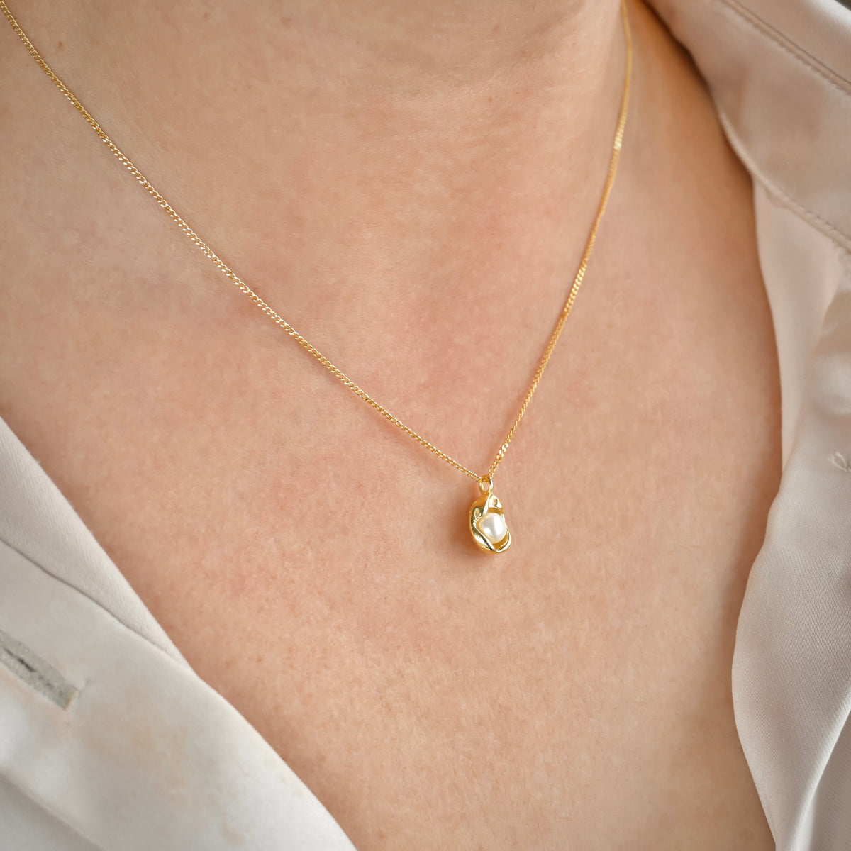 Gold necklace with pearl charm on a person wearing a white blouse.