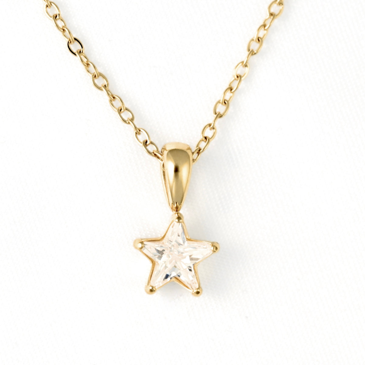 A gold star pendant necklace with a clear faceted gemstone, suspended from a delicate gold chain on a white background.