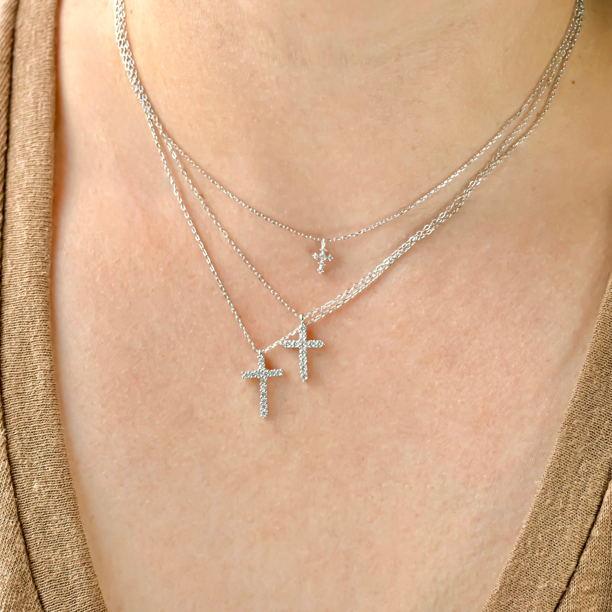 Layered silver diamond cross necklaces with thfree different sizes on a person wearing a gold top.