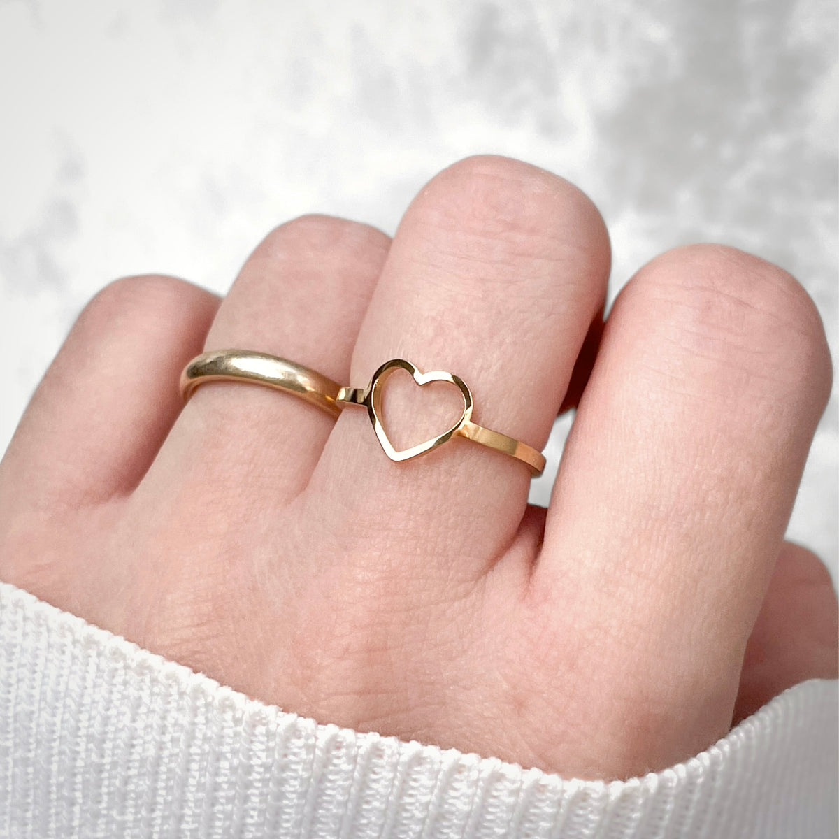 Gold heart-shaped ring on a finger against a white background