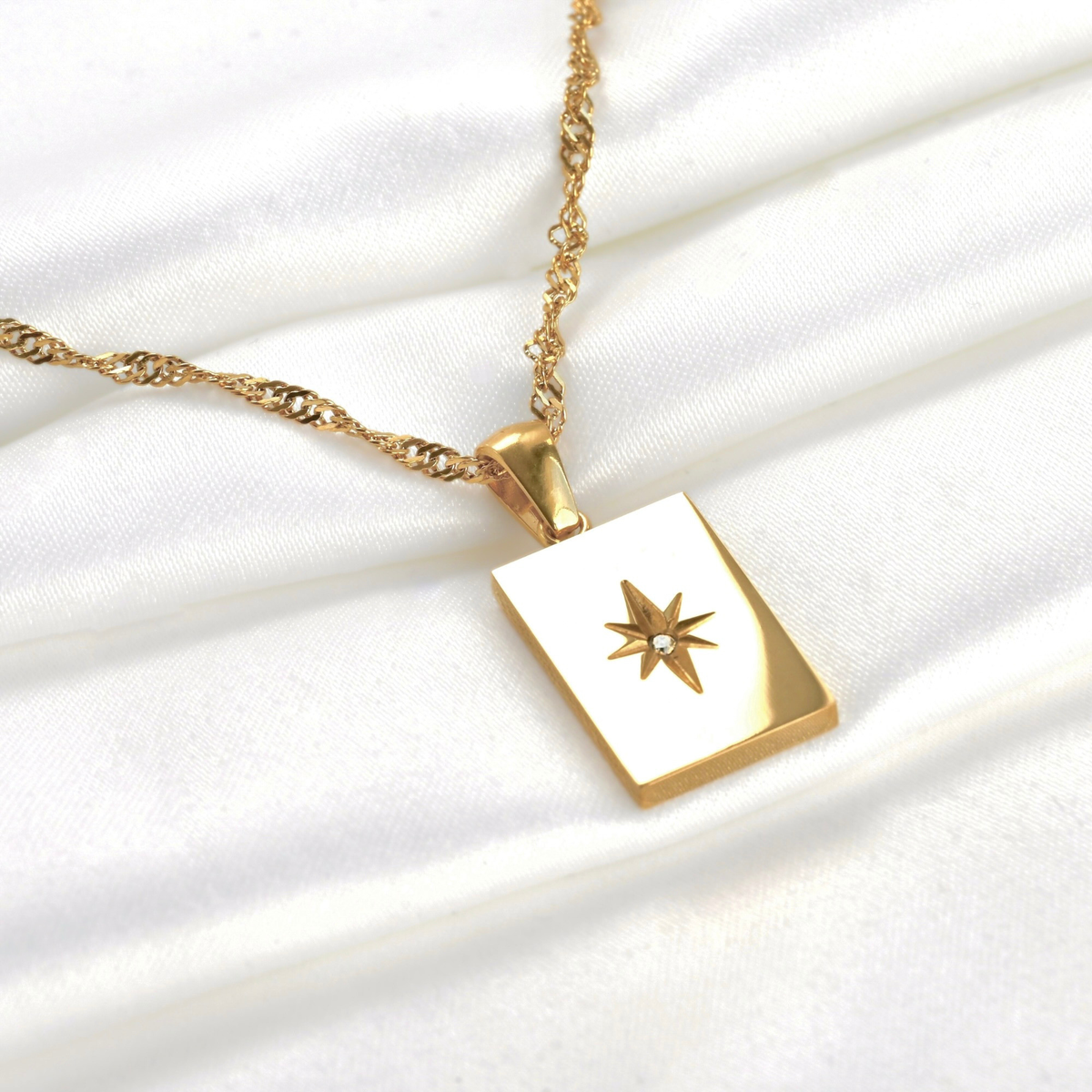 Front view of gold rectangle starburst necklace reflecting light on a white fabric background