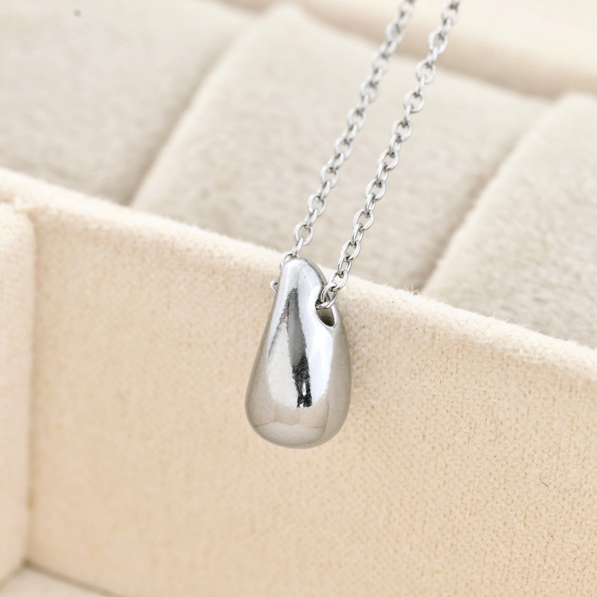 close up of Silver teardrop pendant necklace on a beige cushion