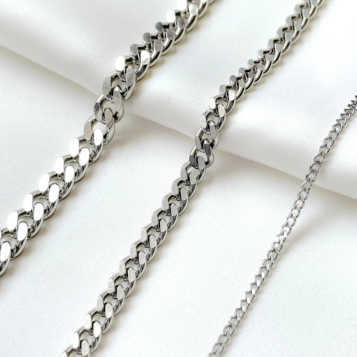 Three silver cuban chains in 2mm, 5mm and 7mm on a white fabric background