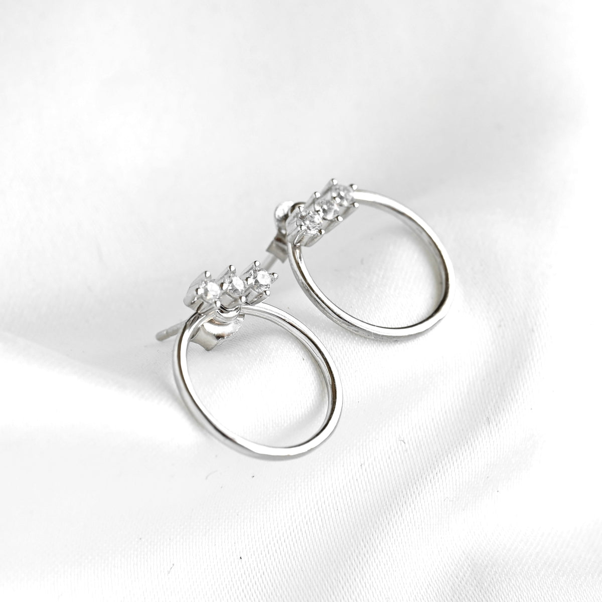 Pair of silver hoop earrings with clear gemstones on a white background