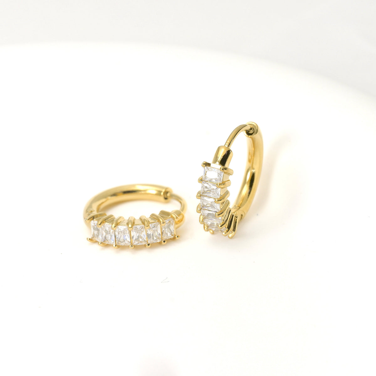 Gold hoop earrings with clear rectangular gemstones on a white background