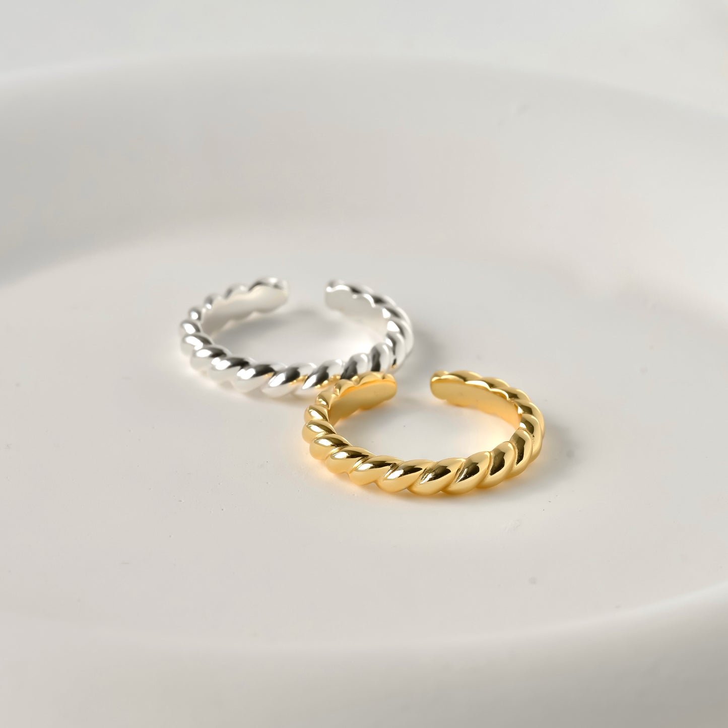 Two gold and silver open rings with a croissant design on a light gray background