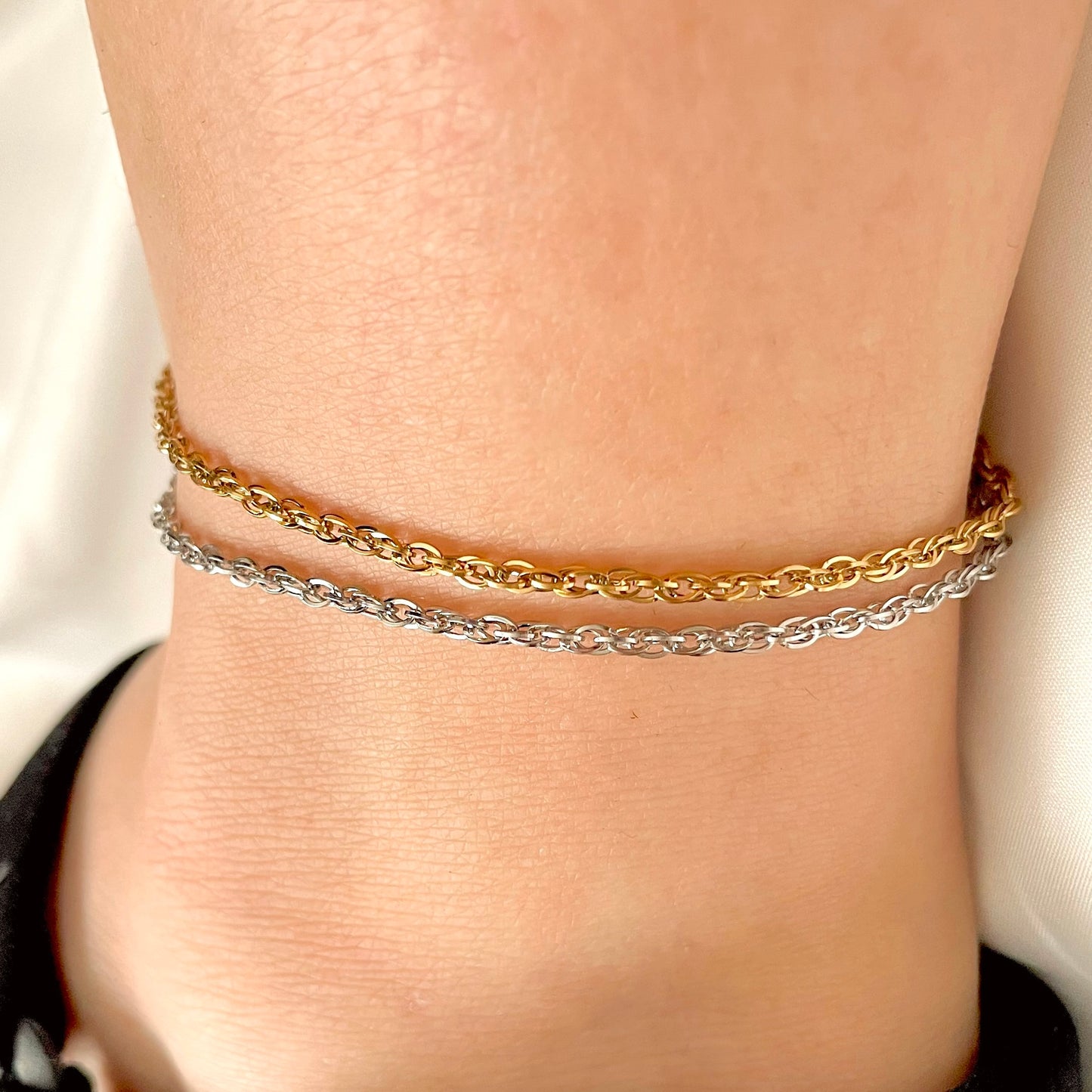 Front view of two gold and silver chain anklets stacked on a person's ankle.