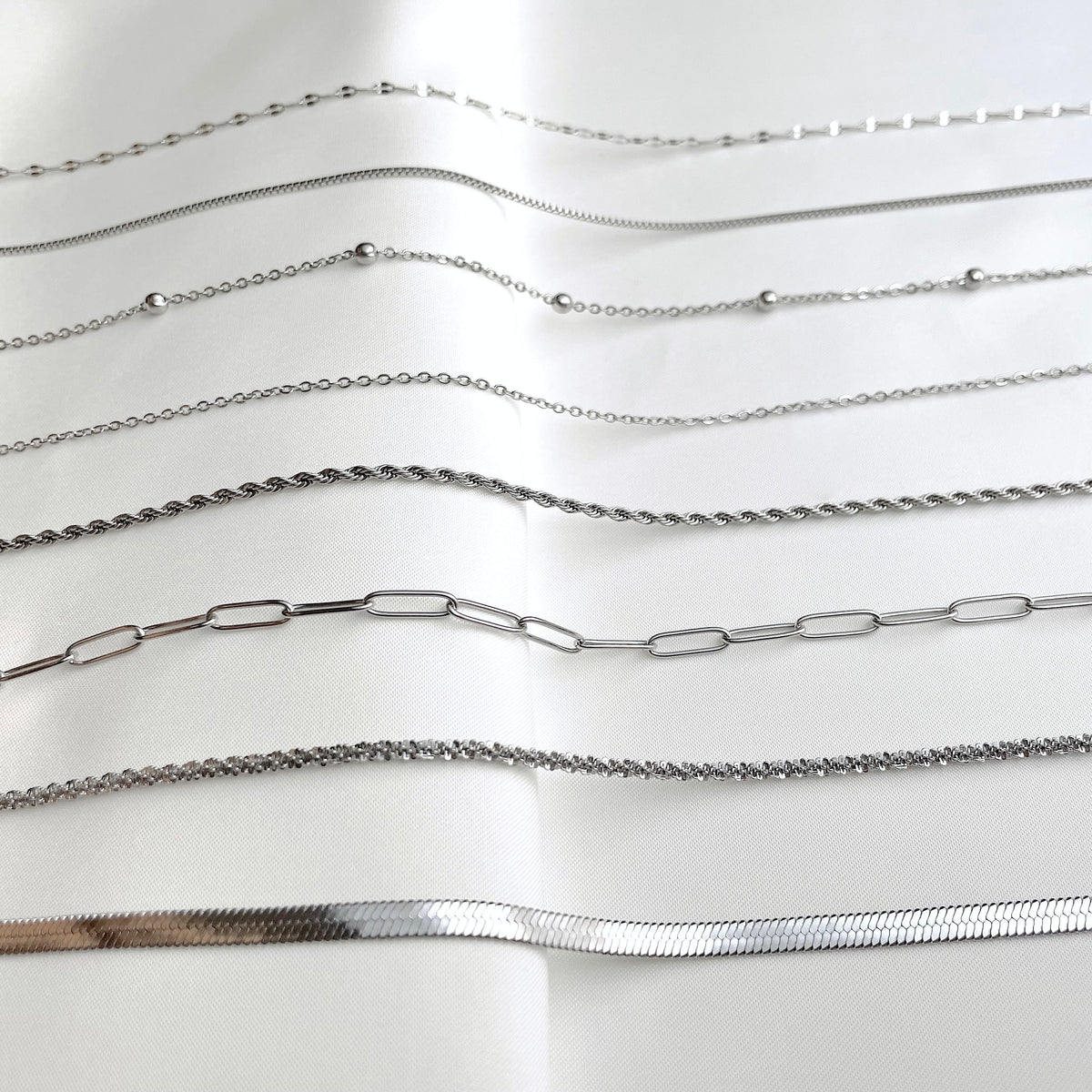 Collection of various silver chains on a white background