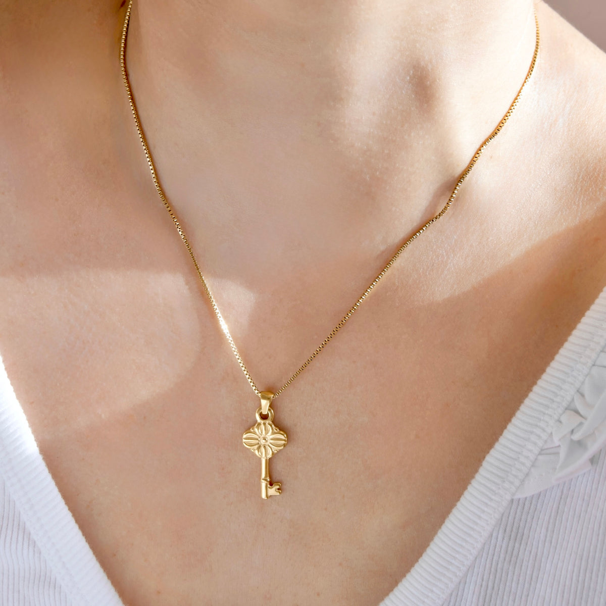 A close-up of a person wearing a delicate gold chain necklace with a small key-shaped pendant, styled with a white ribbed top.