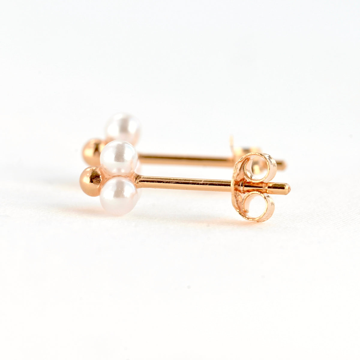 Side view of two rose gold stud earrings with tiny white pearls on a white background