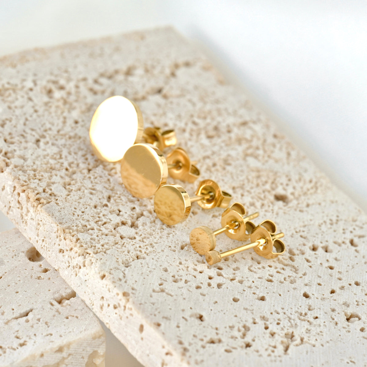 Gold earrings on a textured beige surface