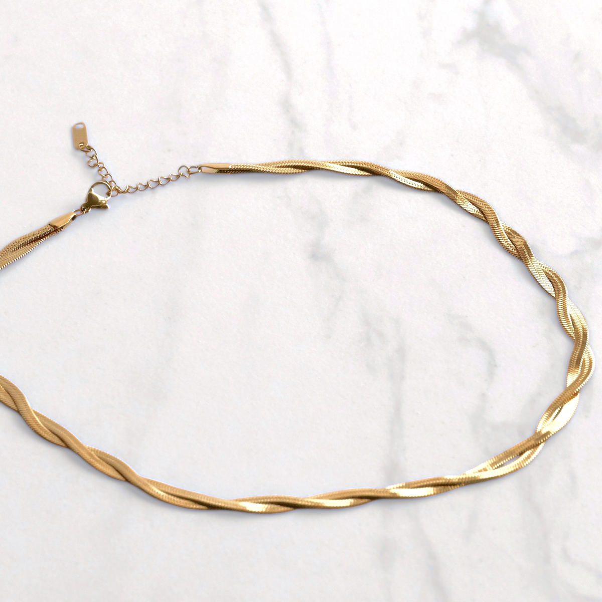 Gold herringbone necklace on a white marble background