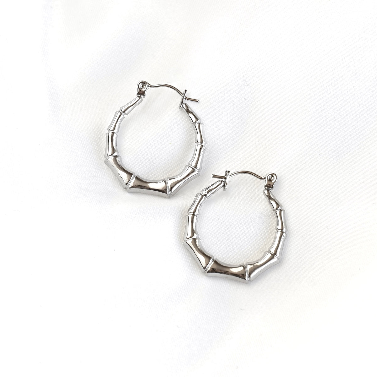 A pair of silver hoop earrings with a textured, segmented design resembling bamboo stalks, displayed on a clean white background.