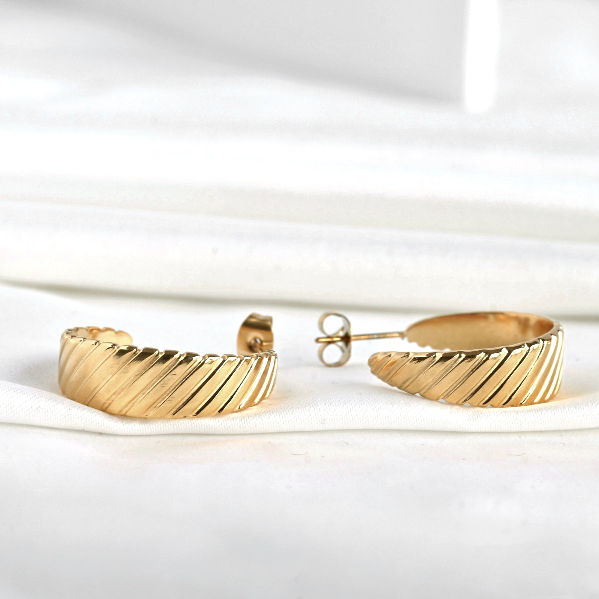 Close-up view of ribbed gold hoop earrings on a white background