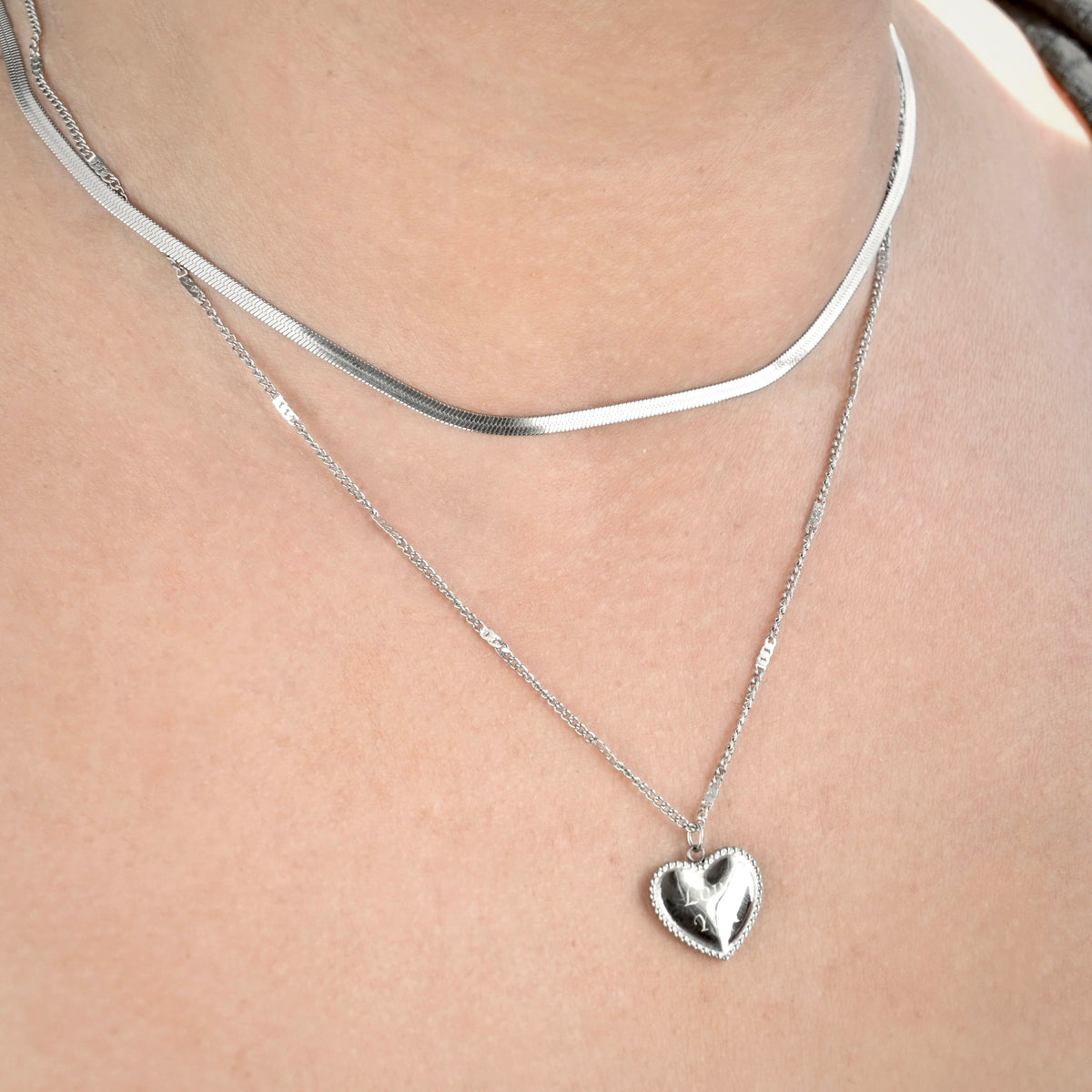 Angled view of silver heart necklace set on a person's neck against a neutral background