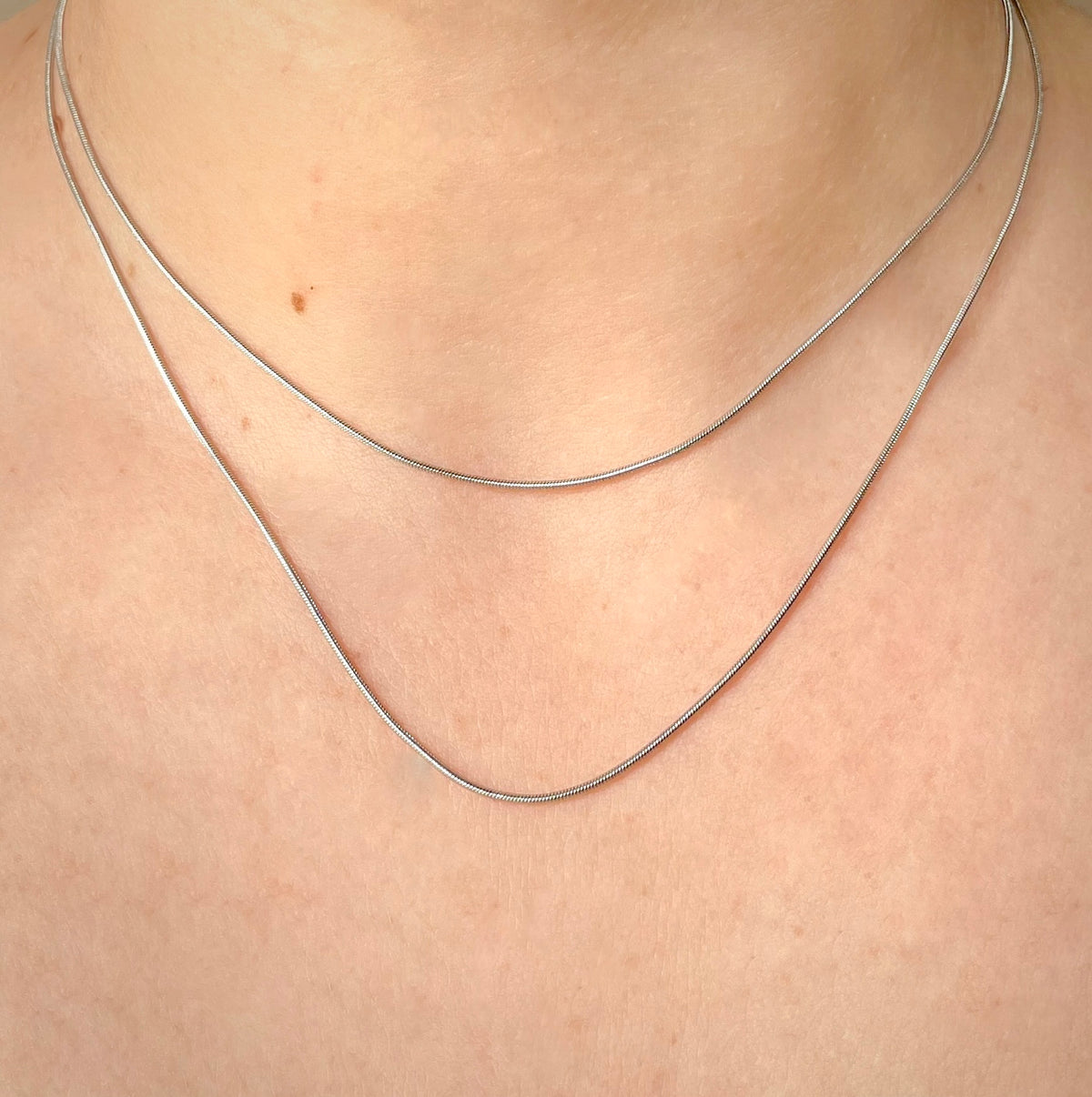Skinny silver snake necklace set on a person's neck