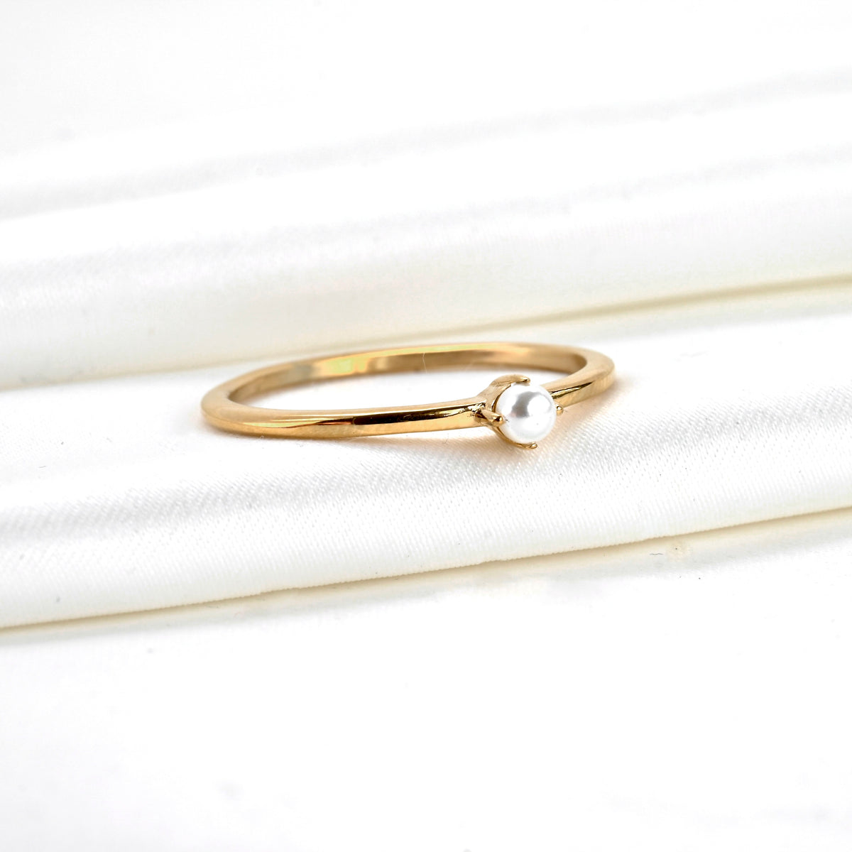 ANgled view of gold ring with a pearl on a white fabric background