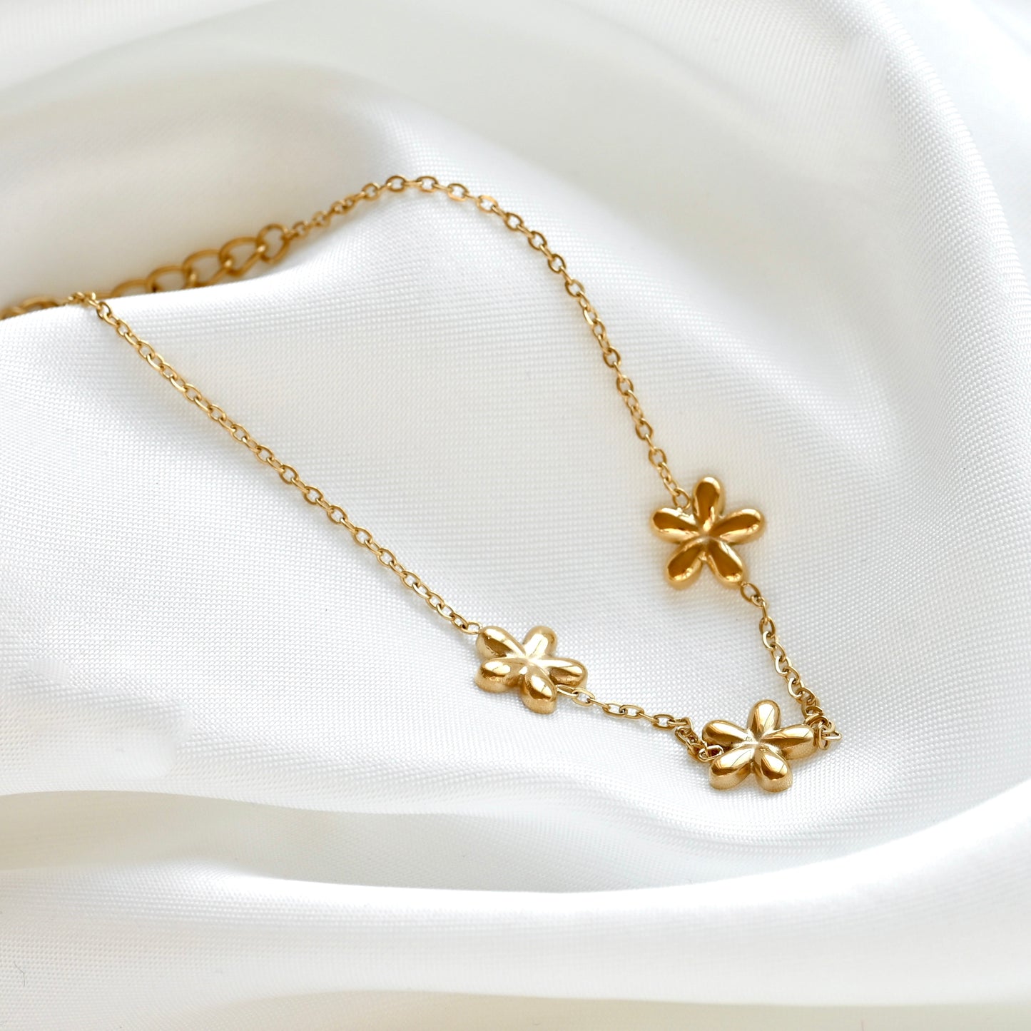 Gold flower trio bracelet on a white satin background