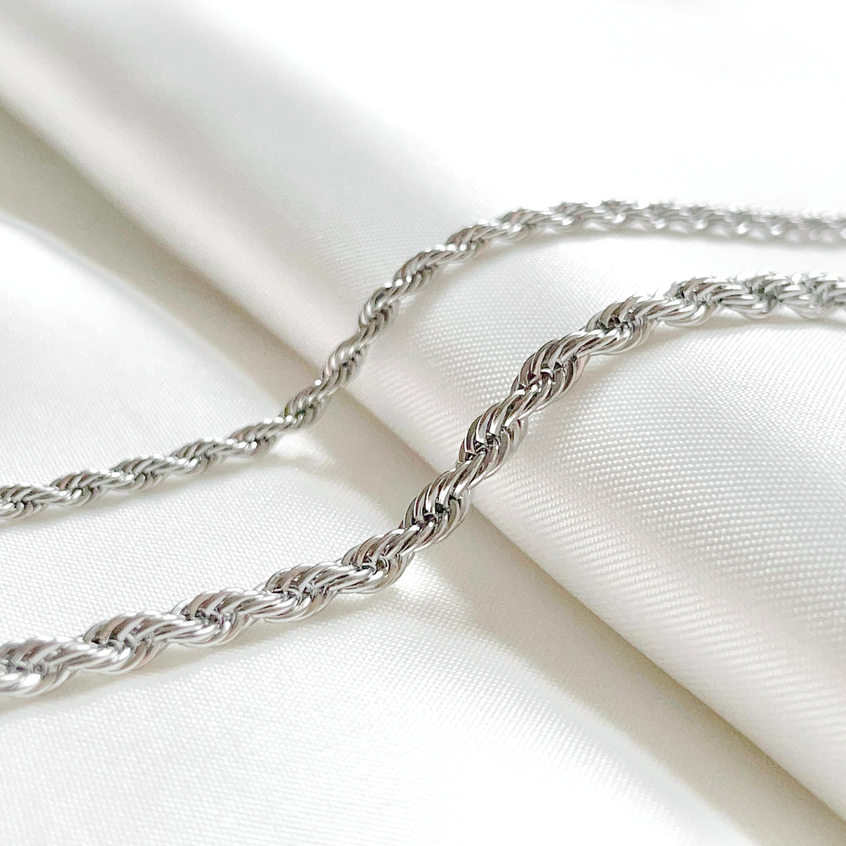 Thin and thick silver rope chains on a white fabric background
