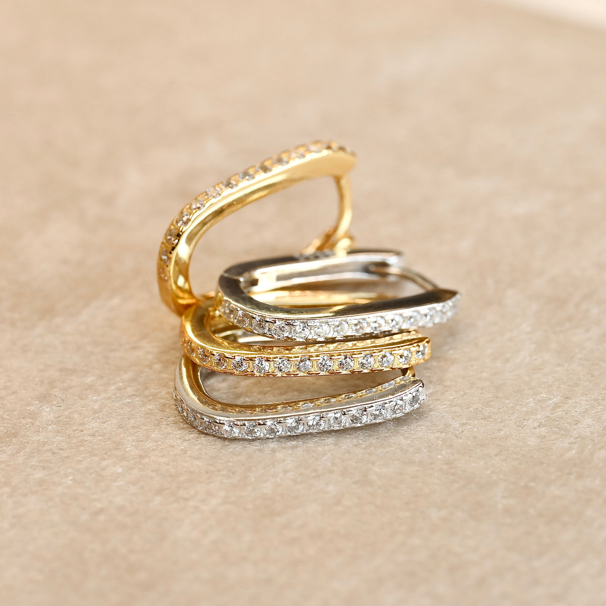 Set of gold and silver U earrings with pave set diamonds stacked on top of each other on a beige background