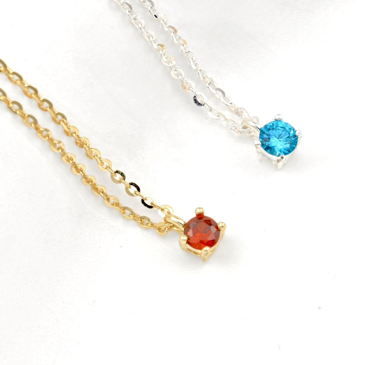 Two necklaces, one gold and one silver with a single gemstone on each on a white background