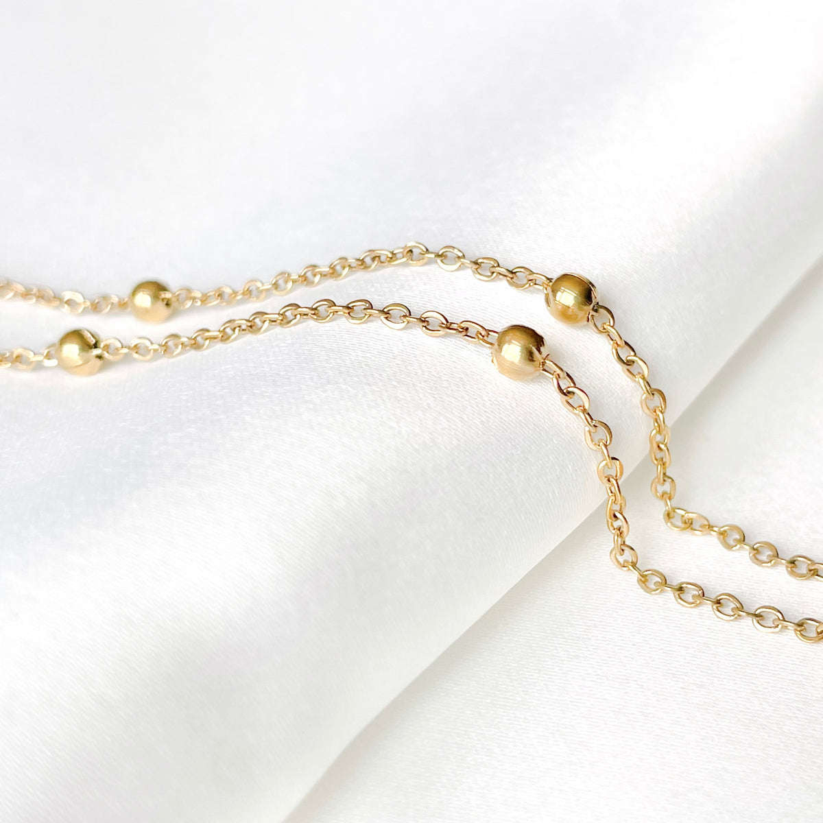 Gold chain necklace with medium sized gold bead stations on a white background