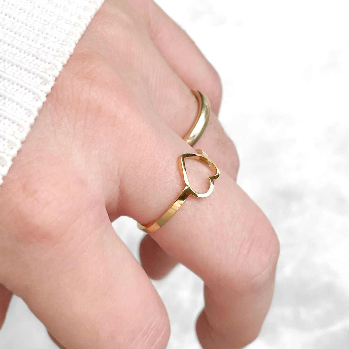 Gold ring with heart design on a finger against a white background