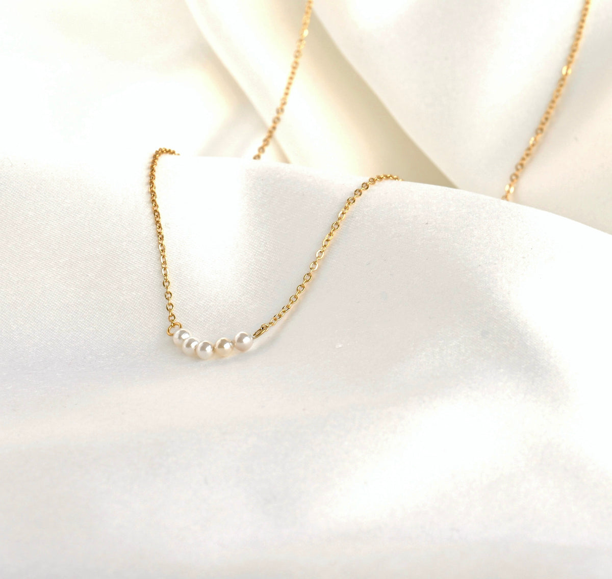 Gold necklace with tiny pearls on a white fabric background