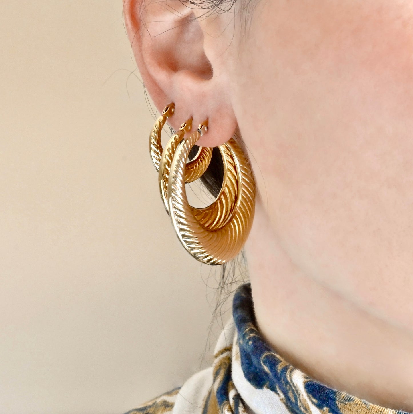 Gold hoop earrings worn by a person with a neutral background
