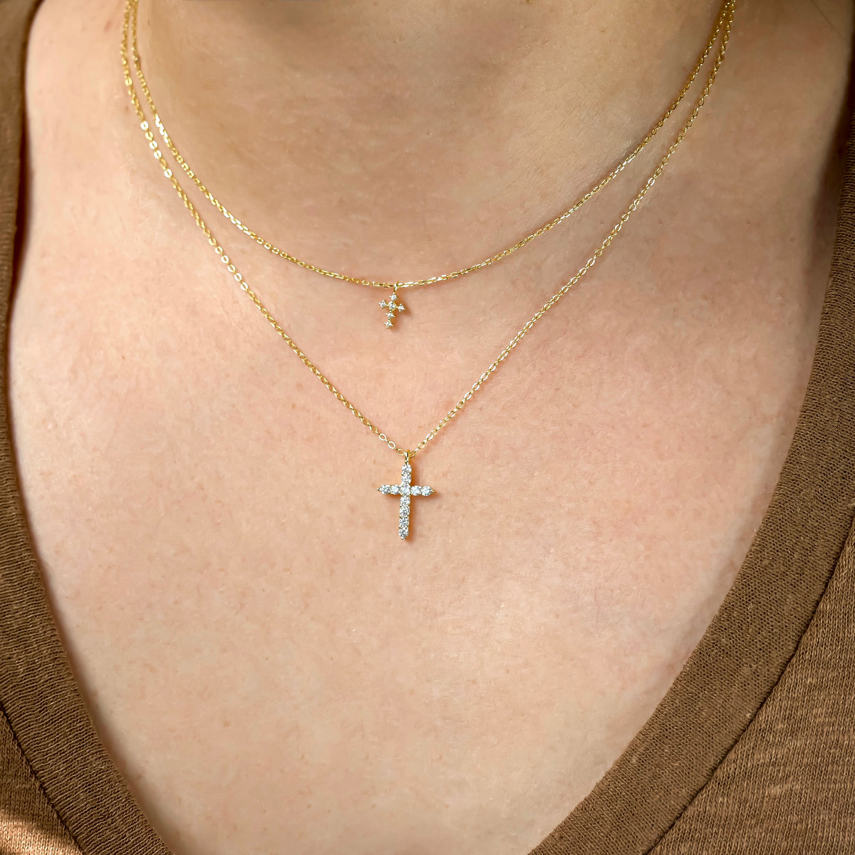 Close-up of a person wearing two gold necklaces, one super tiny and one small sized cross pendants.