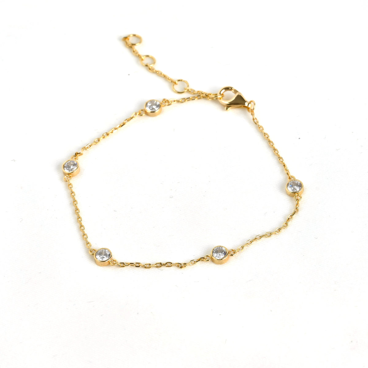 Delicate gold bezel station bracelet with small crystals and a three point extender on a white background