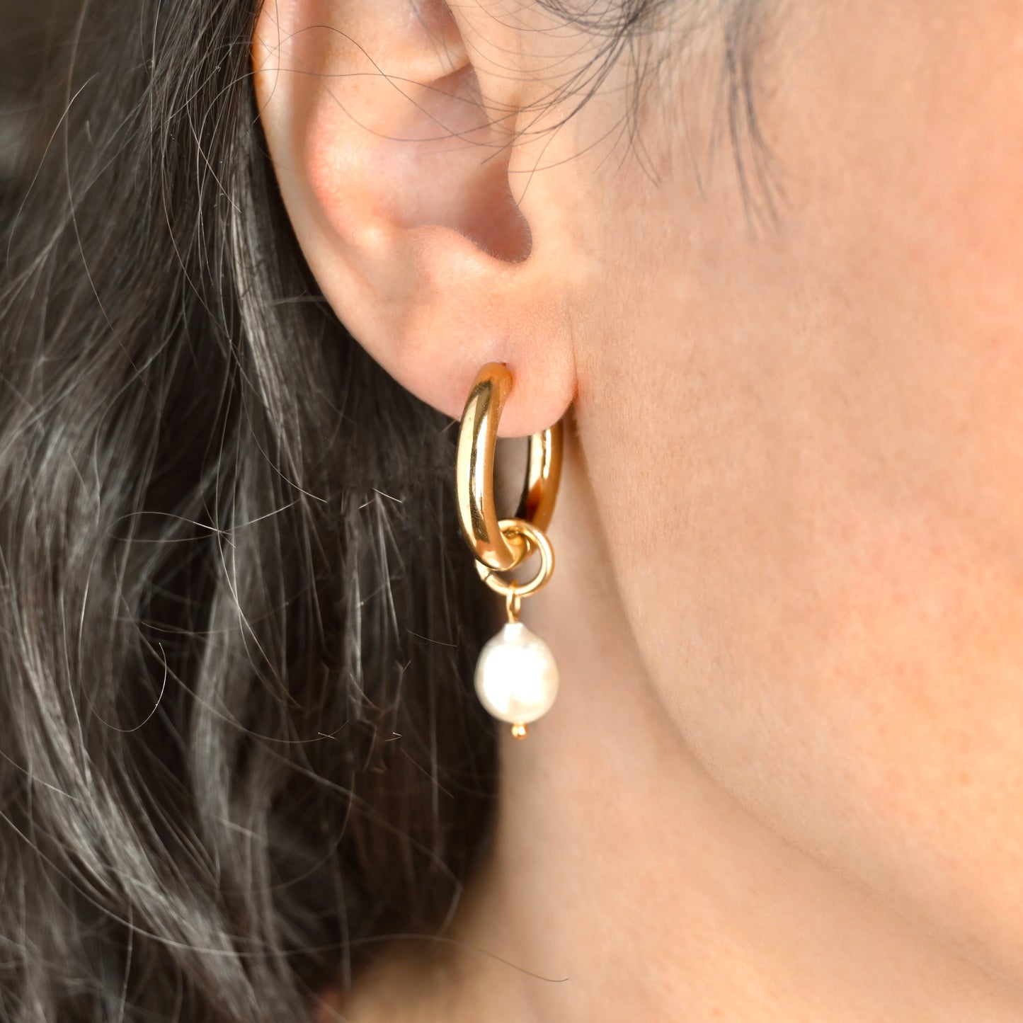 Gold hoop earring with a pearl drop worn by a person