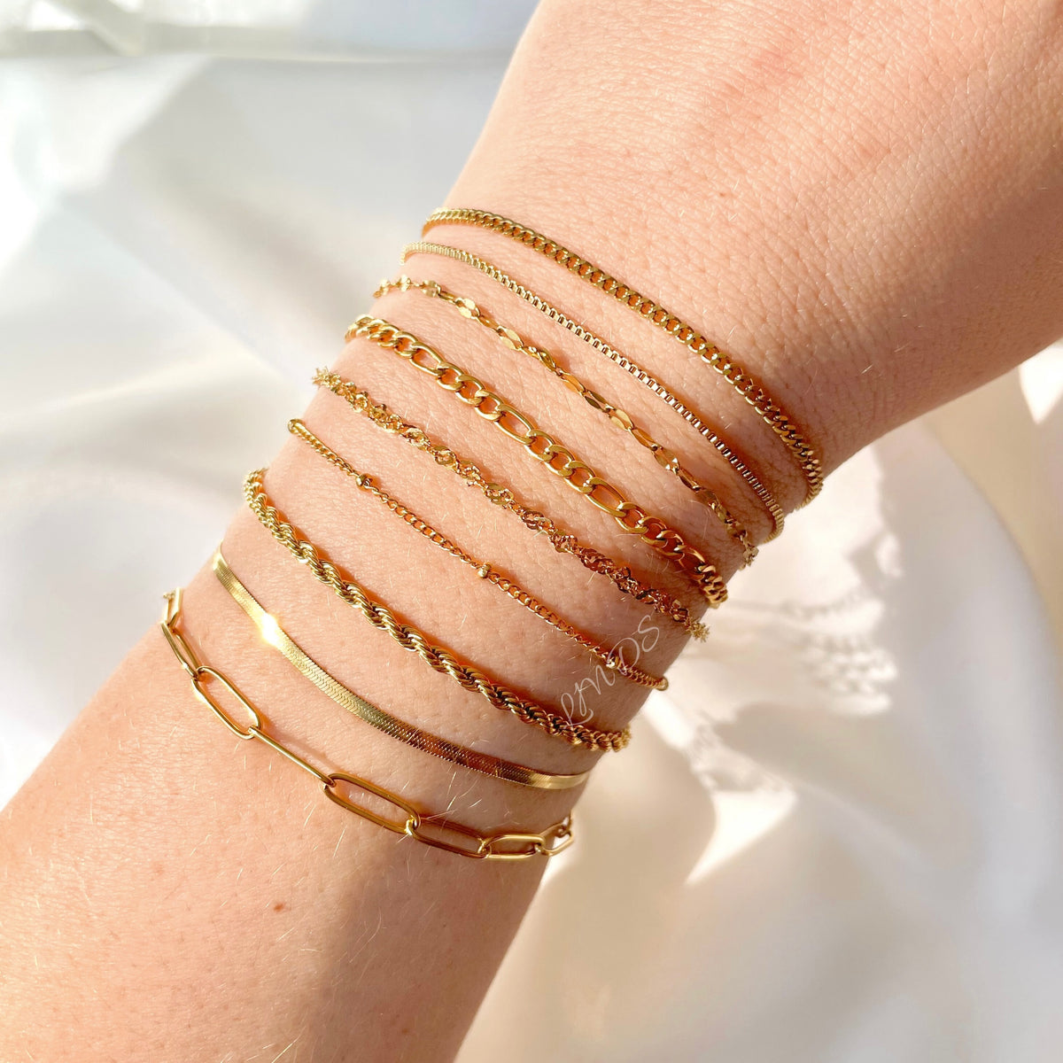 Multiple delicate chain bracelets on a wrist against a light background
