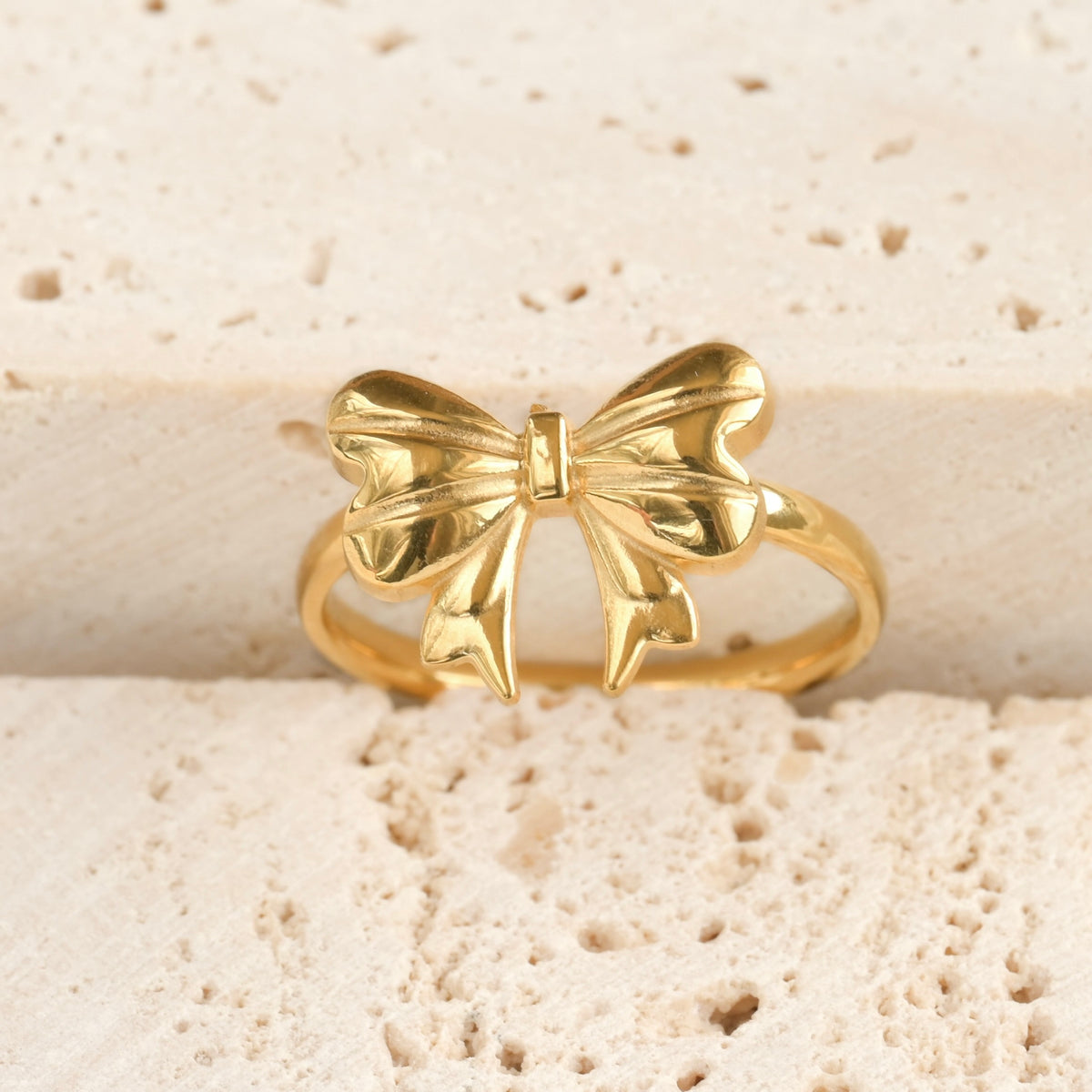 Front view of a gold bow-shaped ring on a textured stone surface