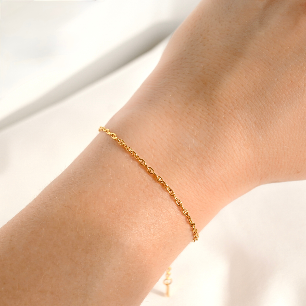A delicate gold chain bracelet worn on a person's wrist, shown in a close-up shot against a soft, light background.
