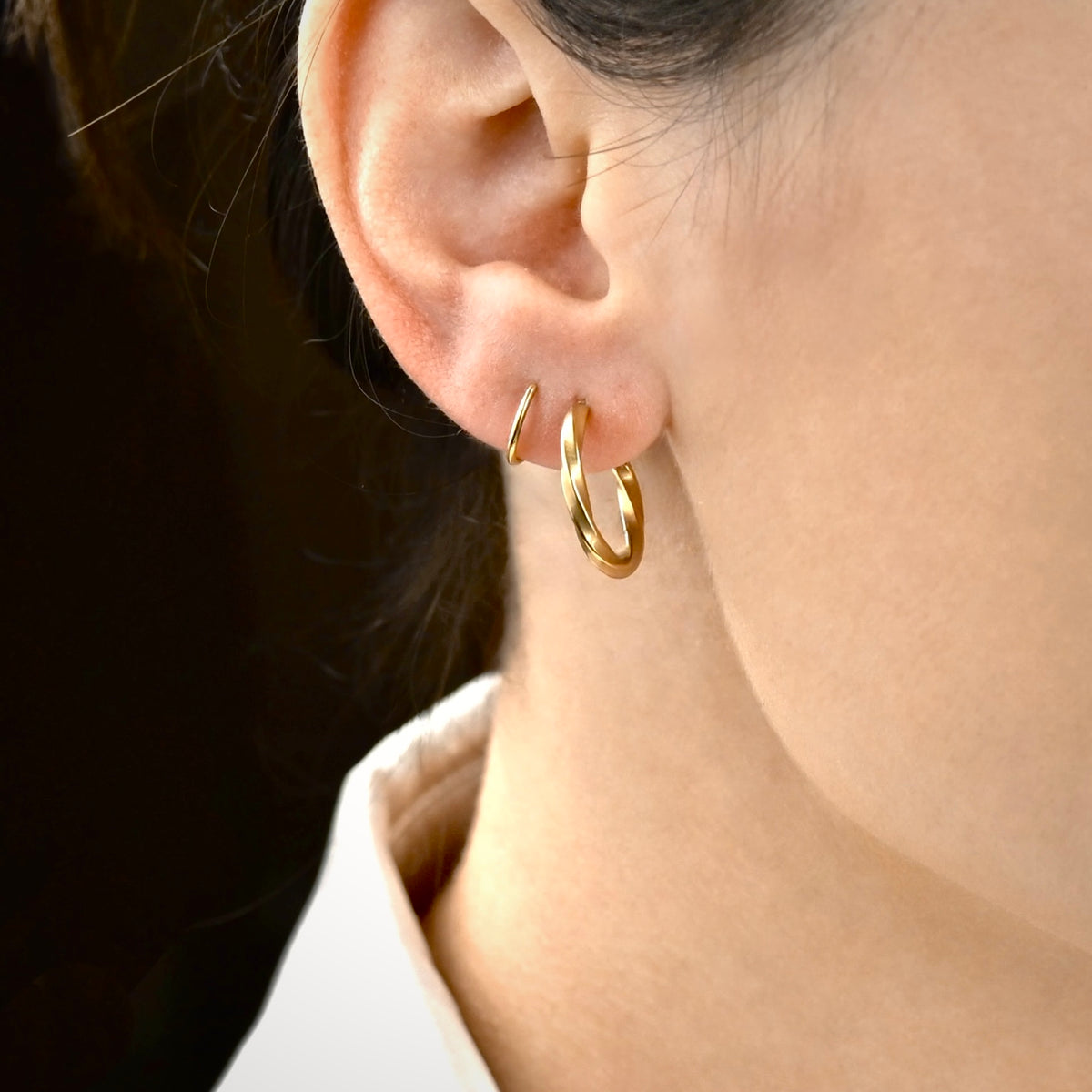 Close-up of a person wearing gold swirl hoop earrings with a blurred background