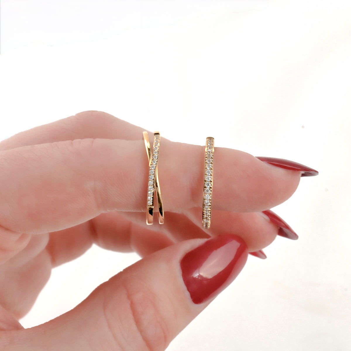 Gold stacking ring set being worn on a finger with red nail polish against a white background