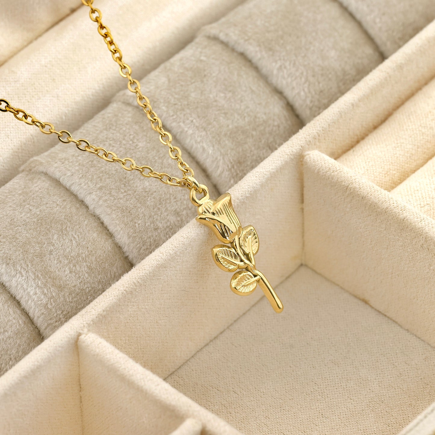Gold necklace with a rose with leafs pendant on a beige quilted surface