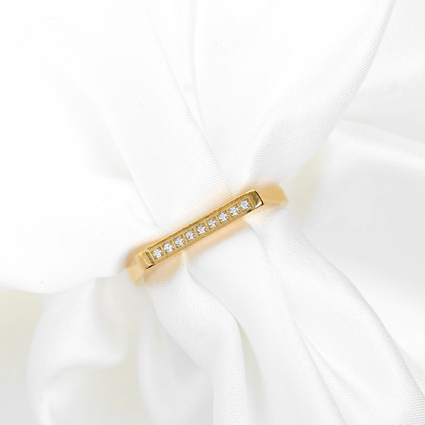 A slim yellow gold band ring with a row of small clear stones, displayed on a soft white fabric drape.