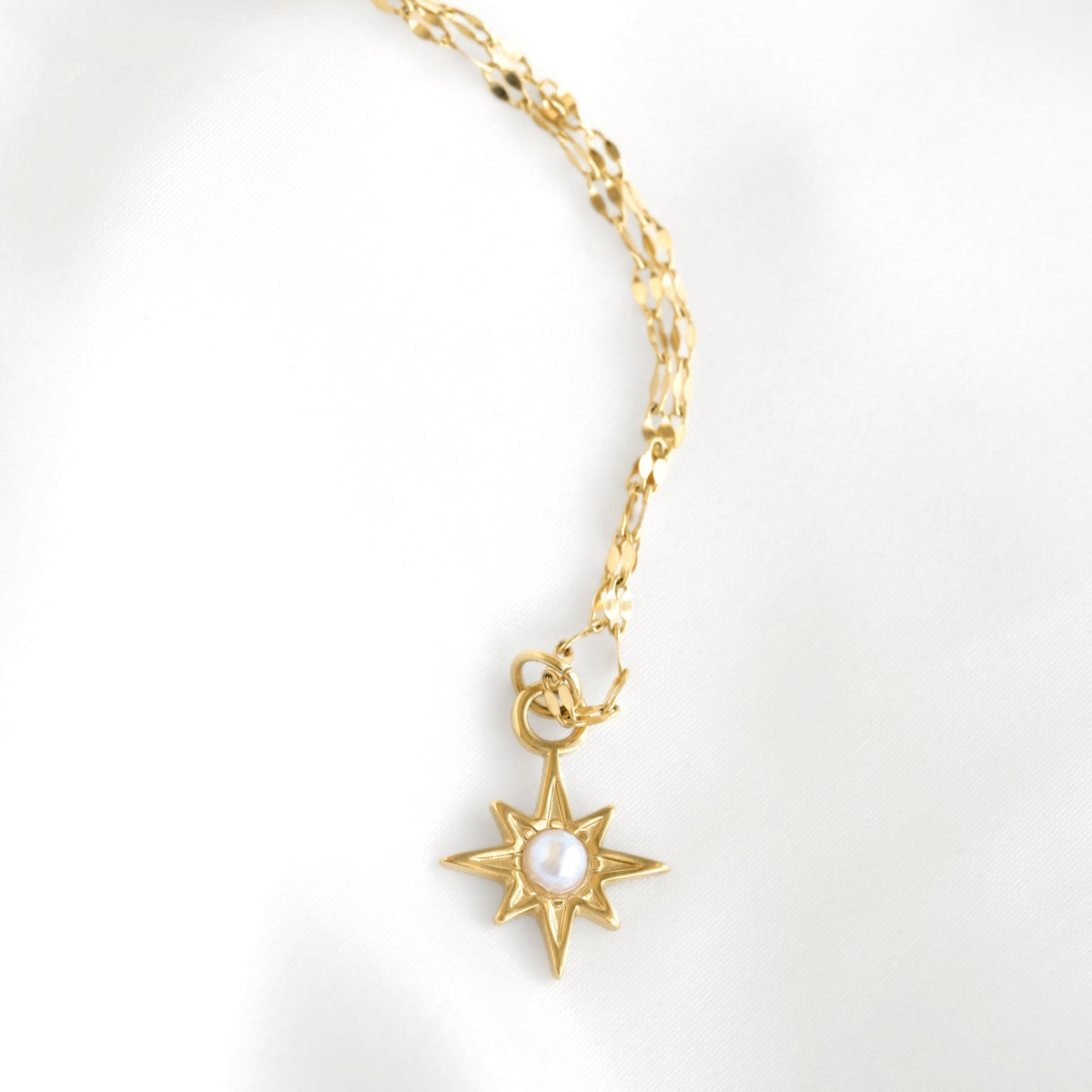 A gold chain necklace featuring a starburst pendant with a central white pearl, displayed on a clean white background.