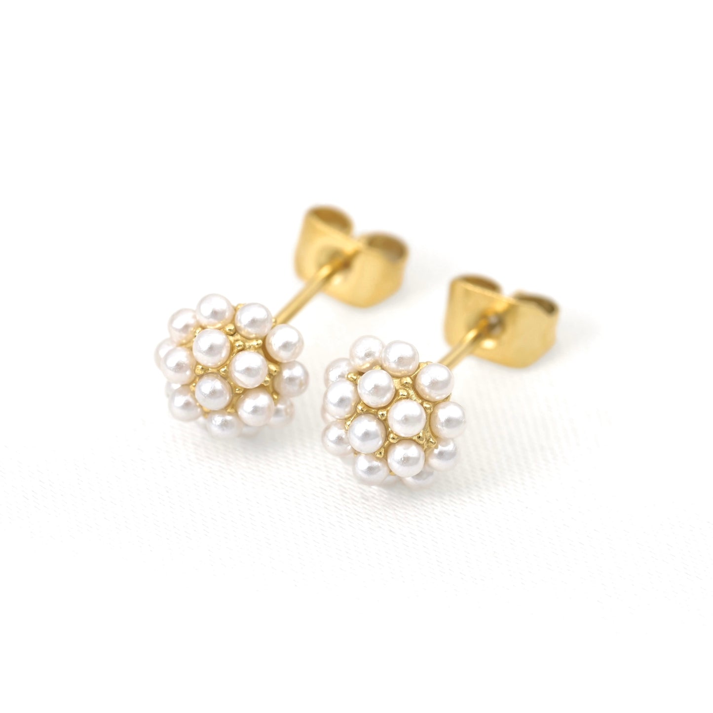 A pair of gold stud earrings featuring small clusters of white imitation pearls, displayed on a clean white textured background.