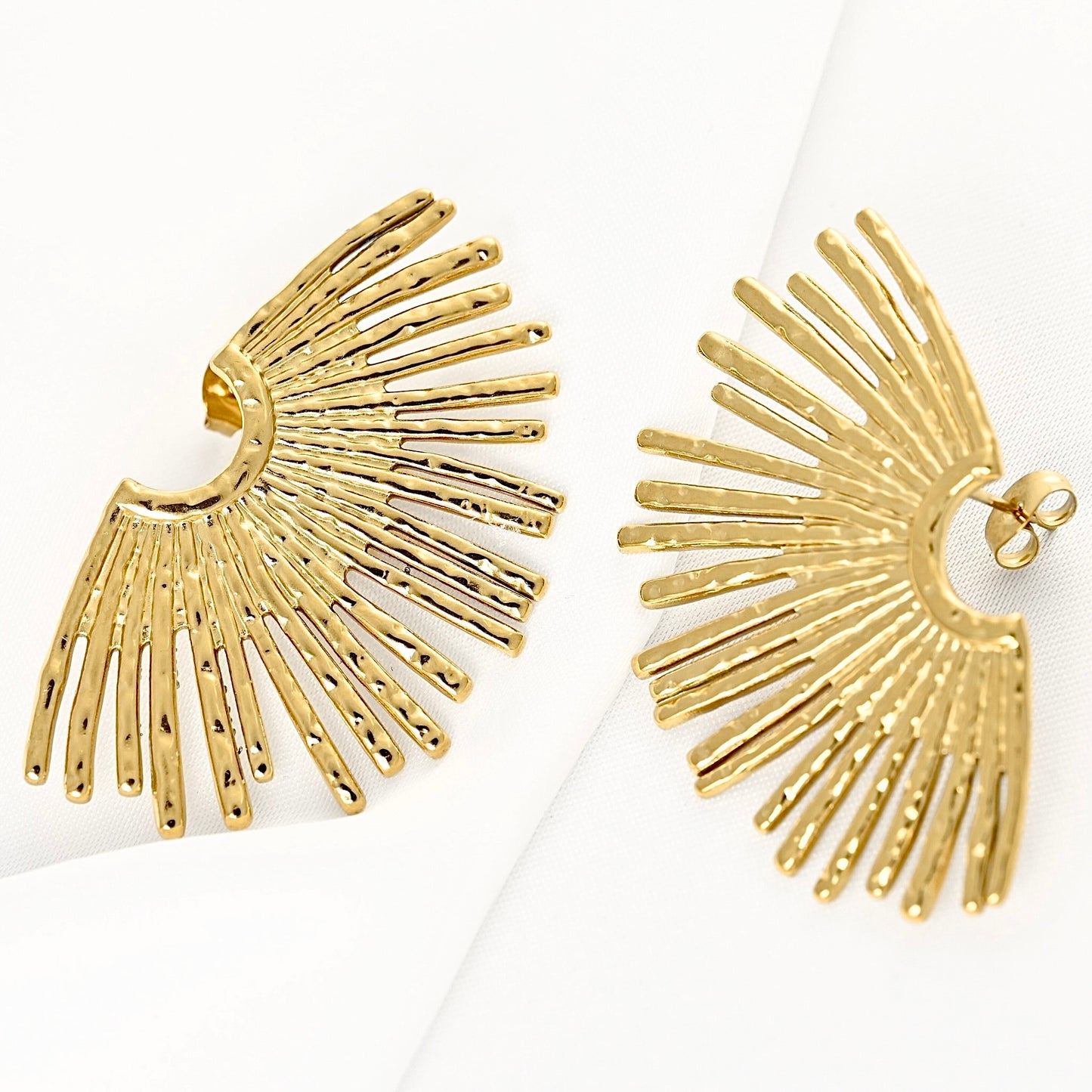 A pair of gold-toned statement earrings with a sunburst or wing-like radiating design, displayed on a clean white background.