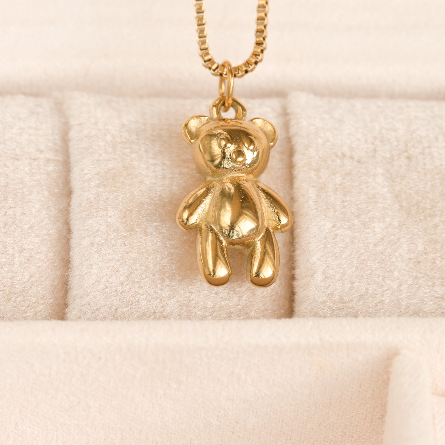 A 16-inch gold-plated teddy bear pendant necklace with a stainless steel finish, displayed on a faux fur surface.