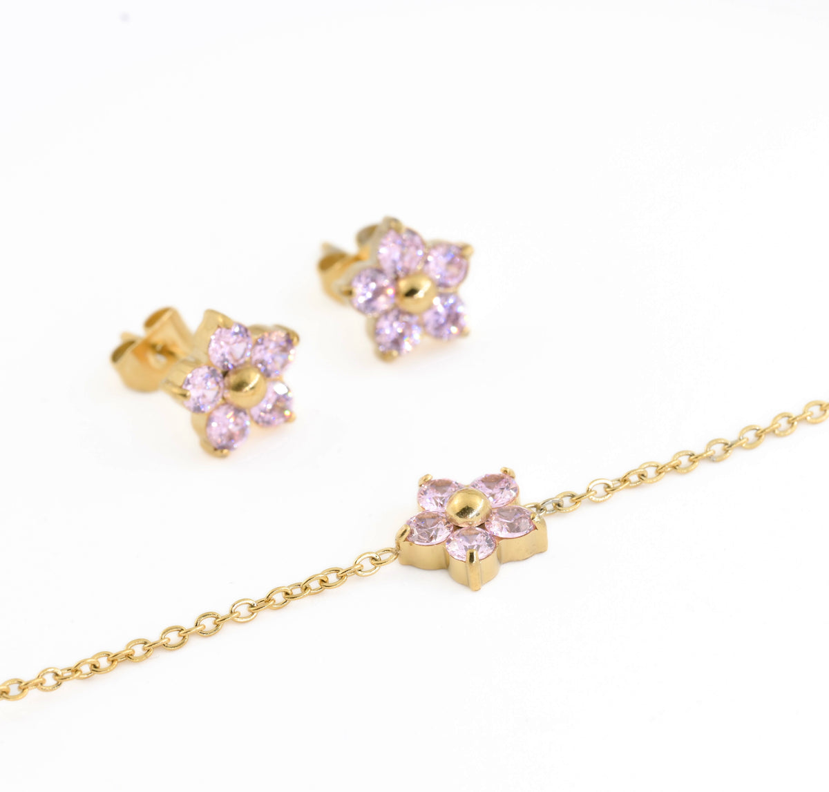 Gold jewelry set including a bracelet and two stud earrings with pink gemstone petals.