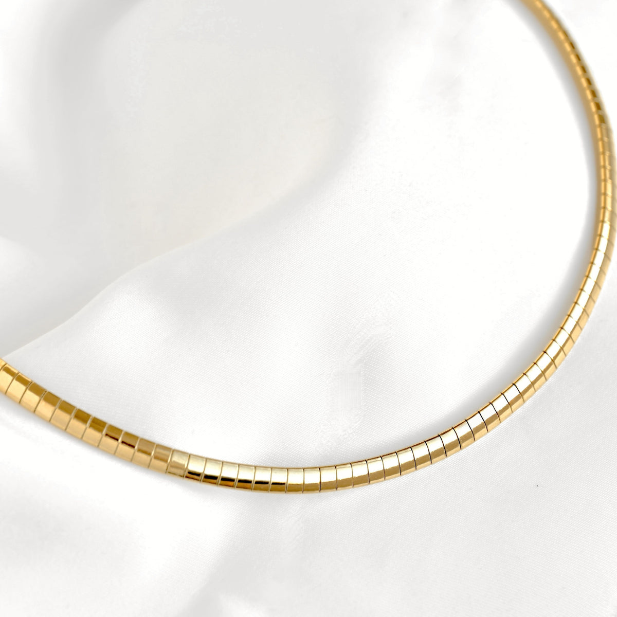 A top close-up view of a gold snake chain necklace draped over a white satin fabric background.
