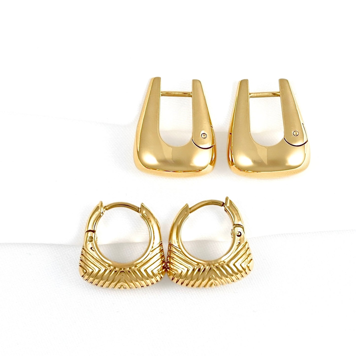 A pair of gold-toned hoop earrings with a textured chevron pattern, shown alongside a pair of matching gold-toned U-shaped hoop backings on a white background.